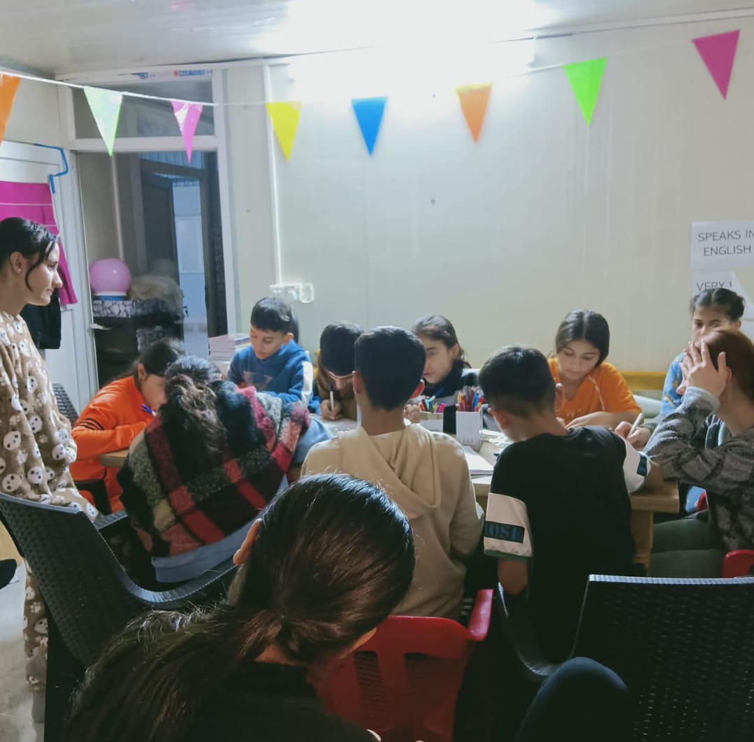 Students gathered around tables in a decorated classroom at Mam Rashan camp